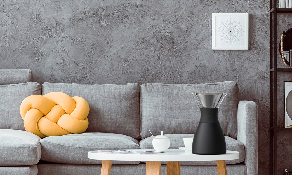 Black clock and posters on dark wall above grey settee with yellow pillow in cozy living room